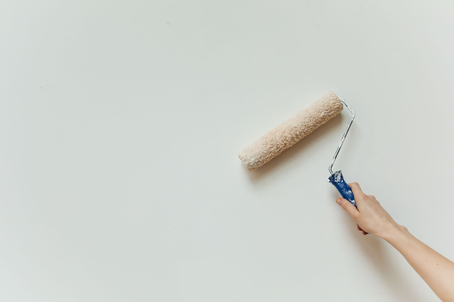 Close-up of a hand painting a wall with a roller brush during renovation.