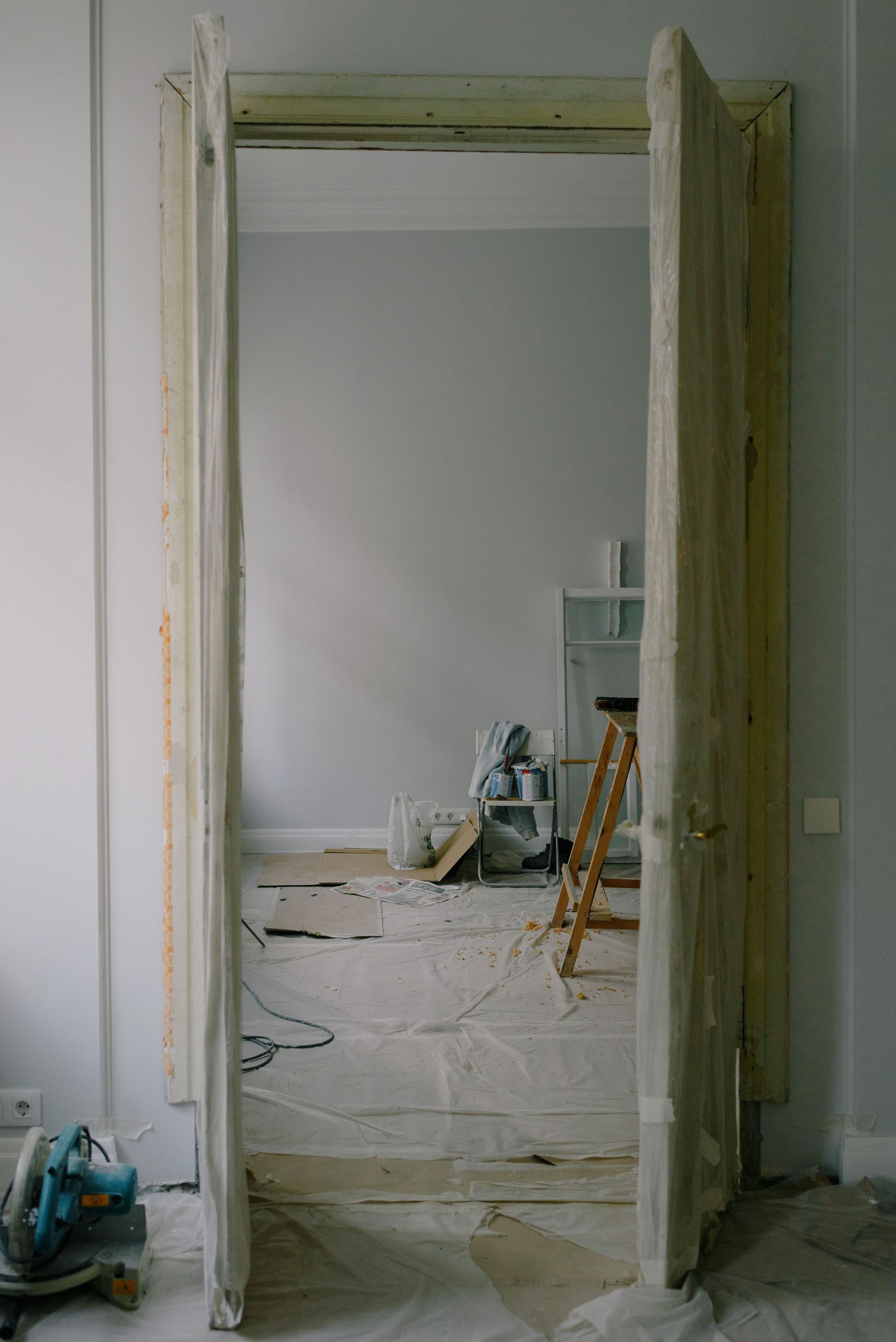 Open door in cellophane with construction materials on floor in room of new flat